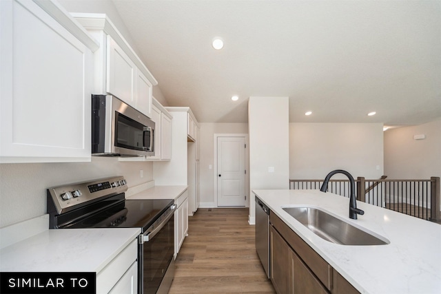 kitchen with light wood finished floors, a sink, white cabinets, appliances with stainless steel finishes, and recessed lighting