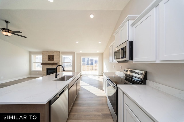 kitchen with a sink, open floor plan, light wood-style floors, stainless steel appliances, and a fireplace