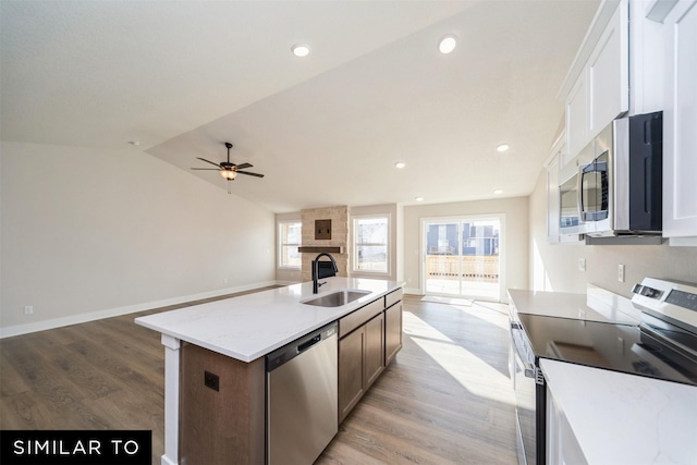 kitchen featuring an island with sink, a sink, open floor plan, light wood-type flooring, and appliances with stainless steel finishes