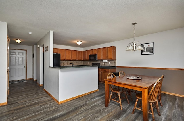 kitchen with dark wood-style flooring, brown cabinets, a chandelier, black appliances, and dark countertops