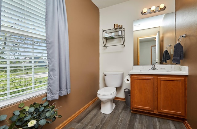 half bath with toilet, baseboards, vanity, and wood finished floors