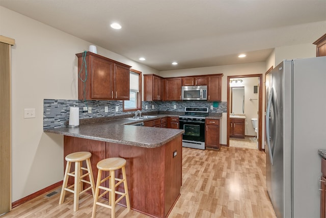 5301 SE 27th St, Des Moines, IA 50320 - kitchen featuring appliances with stainless steel finishes, a peninsula, light wood-style flooring, a sink, and decorative backsplash