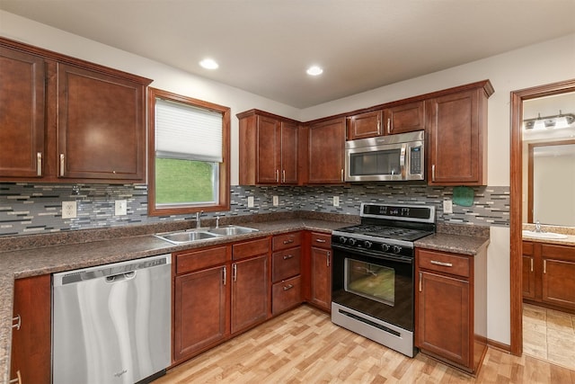5301 SE 27th St, Des Moines, IA 50320 - kitchen featuring appliances with stainless steel finishes, a sink, dark countertops, light wood-style floors, and decorative backsplash