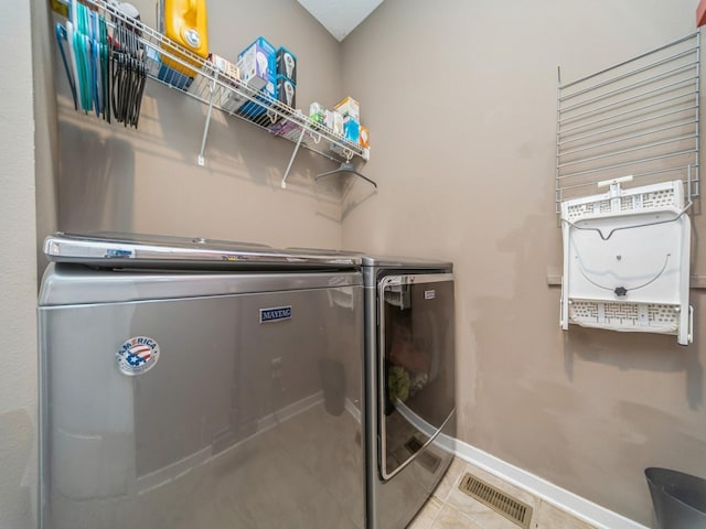 laundry area featuring laundry area, washing machine and clothes dryer, visible vents, tile patterned flooring, and baseboards