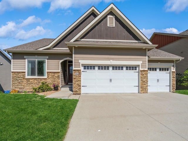 craftsman-style house with board and batten siding, driveway, a front yard, an attached garage, and stone siding