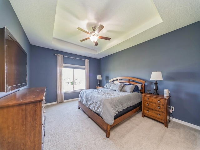 bedroom featuring a tray ceiling, light carpet, baseboards, and a ceiling fan