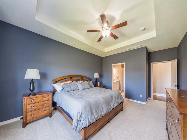 bedroom with connected bathroom, a tray ceiling, visible vents, baseboards, and light colored carpet