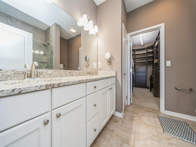 full bath with double vanity, a tile shower, a sink, a walk in closet, and baseboards