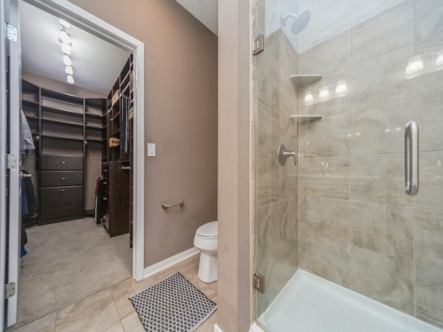 bathroom featuring toilet, a stall shower, tile patterned flooring, a walk in closet, and baseboards