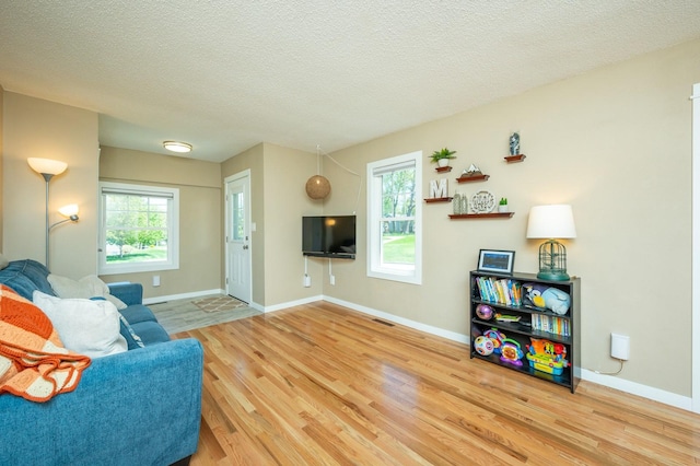 living room featuring a textured ceiling, baseboards, visible vents, and wood finished floors