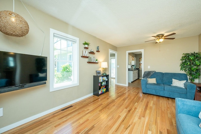 living room featuring ceiling fan, baseboards, visible vents, and wood finished floors