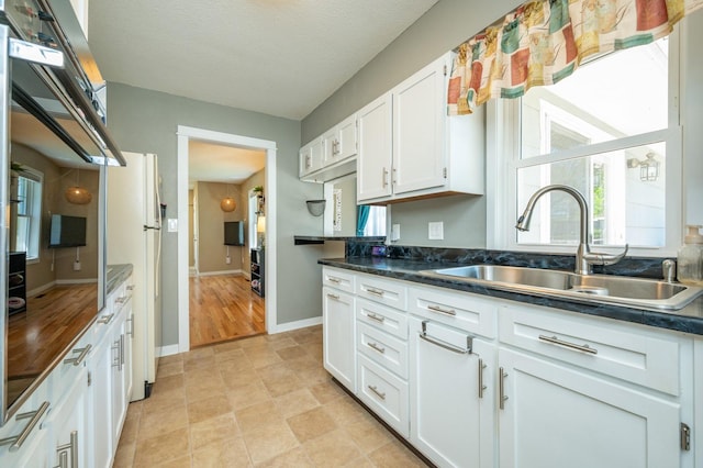 kitchen featuring dark countertops, plenty of natural light, white cabinets, and a sink