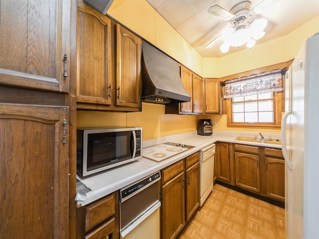 kitchen with a ceiling fan, under cabinet range hood, brown cabinetry, white appliances, and a sink