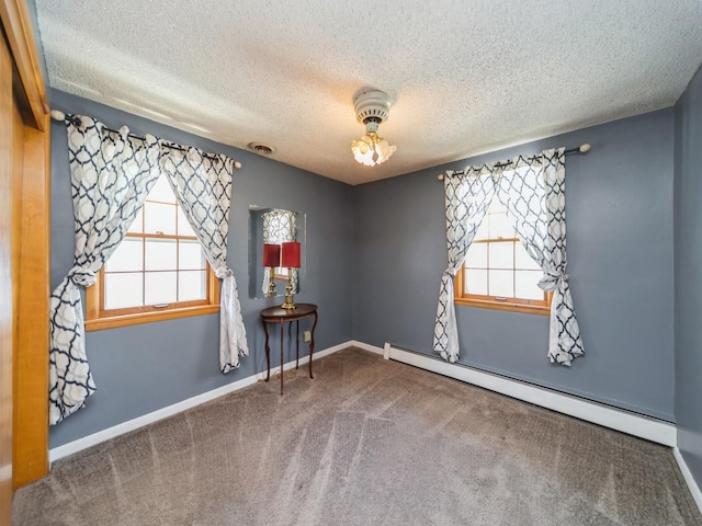 carpeted empty room featuring a textured ceiling, baseboards, a healthy amount of sunlight, and a baseboard heating unit