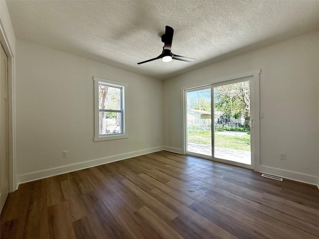 unfurnished room featuring a textured ceiling, visible vents, baseboards, and dark wood-style floors