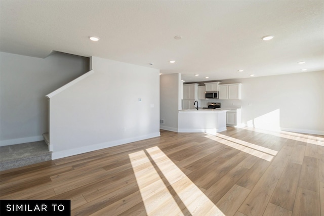 4112 NE 5th St, Ankeny, IA 50021 - unfurnished living room featuring light wood-style flooring, a sink, stairway, baseboards, and recessed lighting