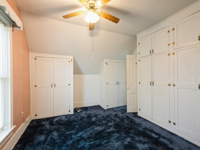 325 W 8th St S, Newton, IA 50208 - unfurnished bedroom with dark carpet, baseboards, lofted ceiling, a ceiling fan, and a textured ceiling
