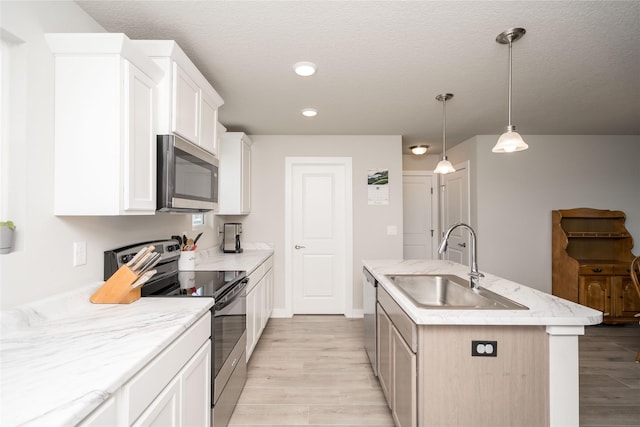 kitchen with a sink, stainless steel appliances, light wood-type flooring, an island with sink, and white cabinetry