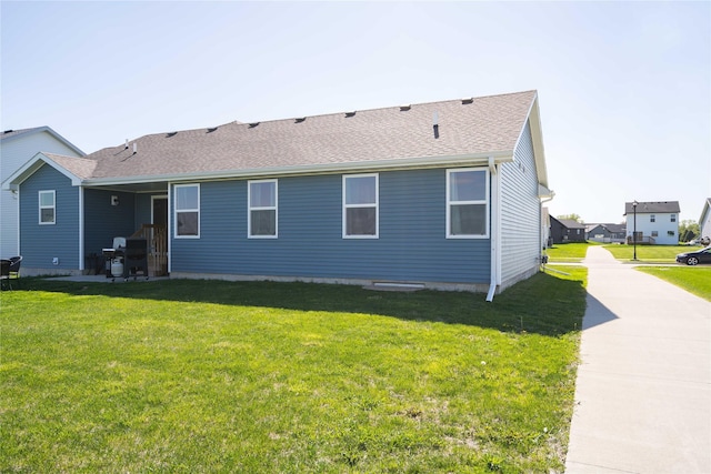 back of house featuring a shingled roof and a lawn