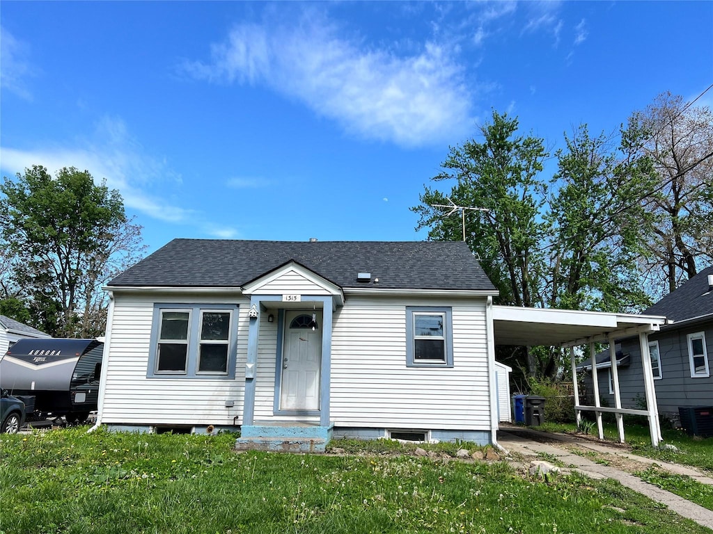 bungalow-style home with central air condition unit, an attached carport, a shingled roof, and a front yard