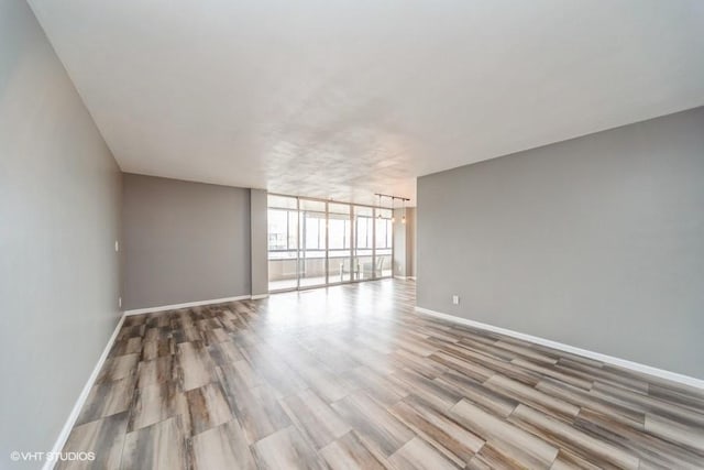 spare room featuring floor to ceiling windows, wood finished floors, and baseboards