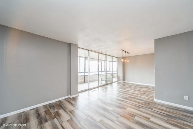 empty room featuring baseboards, a chandelier, expansive windows, and wood finished floors