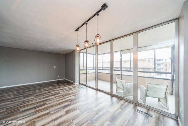 empty room with a wealth of natural light, visible vents, wood finished floors, and baseboards