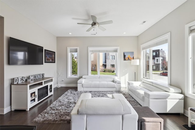 living room featuring a ceiling fan, baseboards, a healthy amount of sunlight, and dark wood finished floors