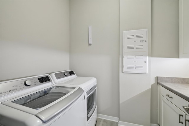 clothes washing area with separate washer and dryer, light wood finished floors, cabinet space, and baseboards