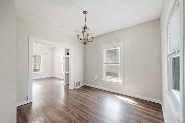 unfurnished dining area with baseboards, dark wood finished floors, an inviting chandelier, and a textured ceiling