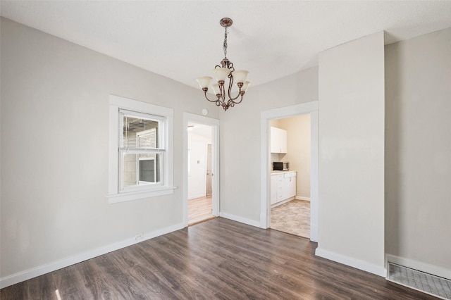 unfurnished dining area with a chandelier, dark wood-style flooring, baseboards, and visible vents