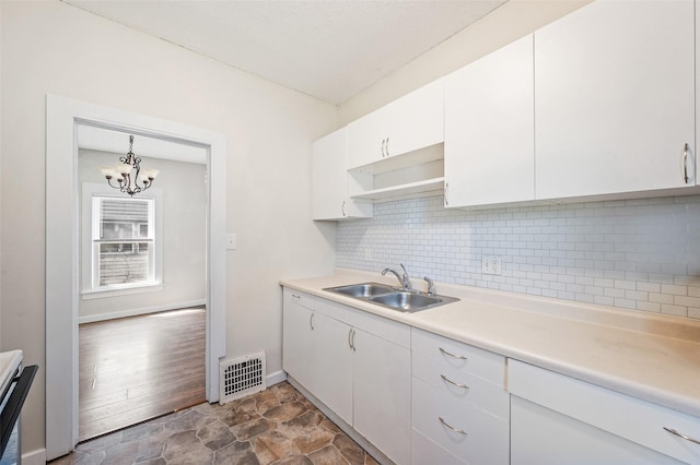 kitchen featuring visible vents, a sink, white cabinetry, backsplash, and light countertops