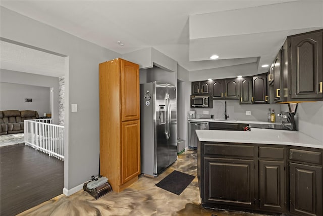 kitchen with a peninsula, a sink, open floor plan, light countertops, and appliances with stainless steel finishes