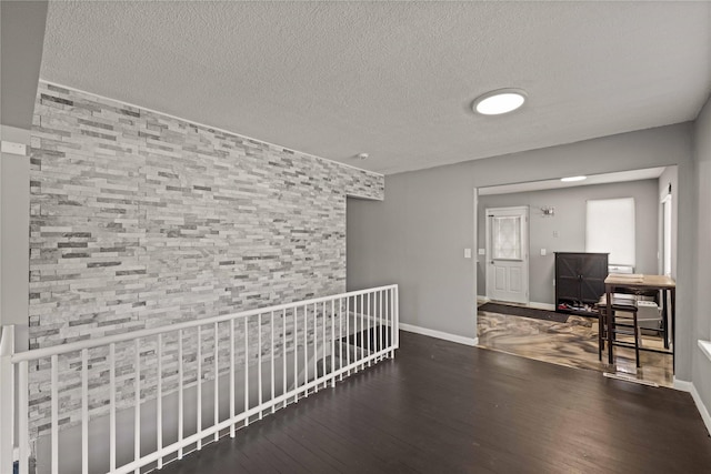 corridor featuring a textured ceiling, wood finished floors, and baseboards