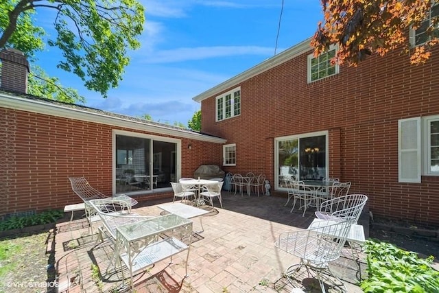 back of property featuring a patio, outdoor dining space, and brick siding