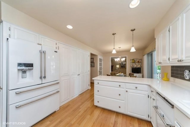 kitchen with white cabinetry, a peninsula, an inviting chandelier, and white refrigerator with ice dispenser