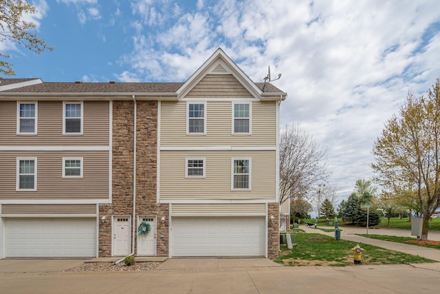 multi unit property featuring stone siding, an attached garage, and driveway