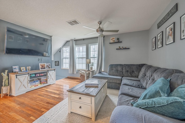living area with a textured ceiling, visible vents, ceiling fan, light wood-style floors, and lofted ceiling