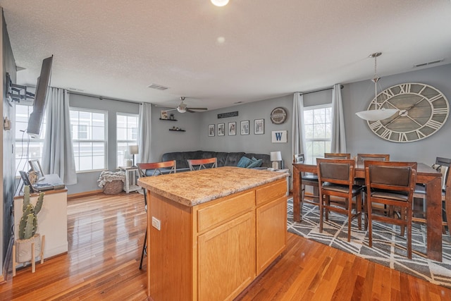 kitchen with light wood finished floors, light countertops, a center island, open floor plan, and a ceiling fan