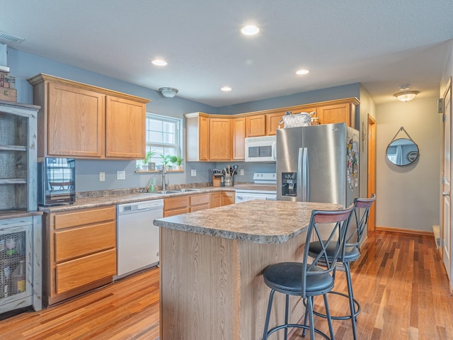 kitchen featuring recessed lighting, a breakfast bar, white appliances, a sink, and light wood-style floors