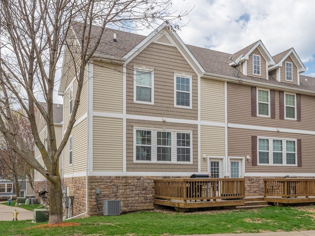 back of house featuring central AC unit, roof with shingles, a deck, and stone siding