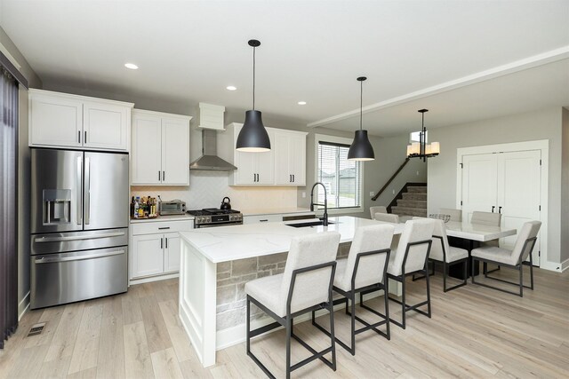 730 NE Country Meadow Dr, Ankeny, IA 50021 - kitchen featuring appliances with stainless steel finishes, a sink, wall chimney range hood, light wood-style flooring, and a center island with sink
