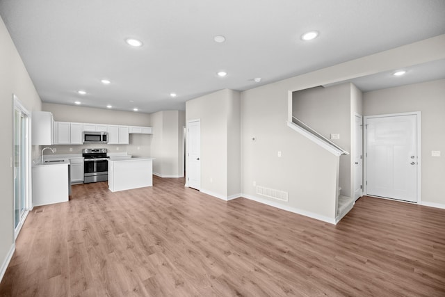 unfurnished living room with recessed lighting, light wood-type flooring, a sink, baseboards, and stairs