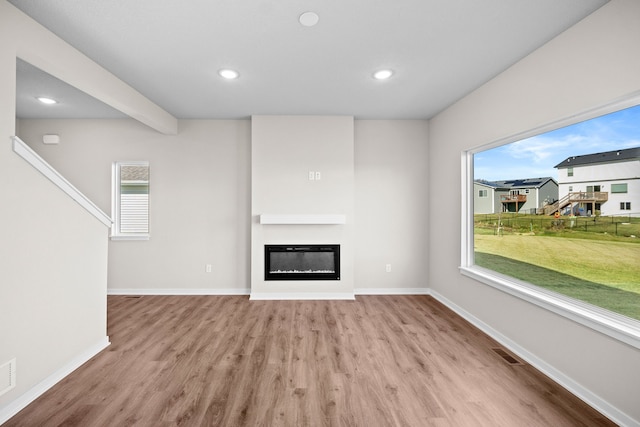 unfurnished living room featuring wood finished floors, a glass covered fireplace, recessed lighting, and baseboards