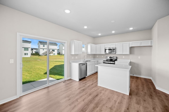 kitchen with appliances with stainless steel finishes, a sink, baseboards, light wood-type flooring, and white cabinetry
