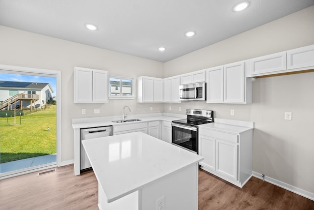 kitchen featuring appliances with stainless steel finishes, a sink, white cabinets, a center island, and light wood-style floors