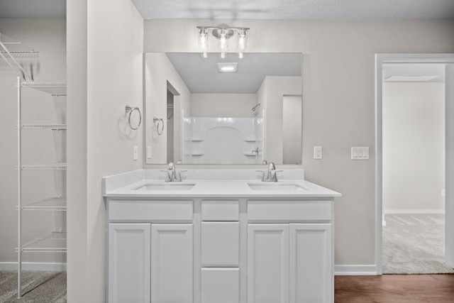 bathroom with double vanity, baseboards, a spacious closet, a shower, and wood finished floors