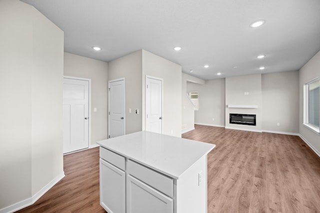 kitchen featuring light wood-style flooring, a center island, recessed lighting, baseboards, and light countertops