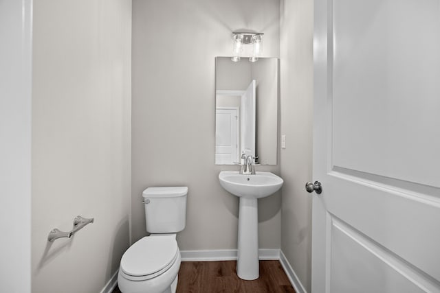 half bath with toilet, wood finished floors, and baseboards