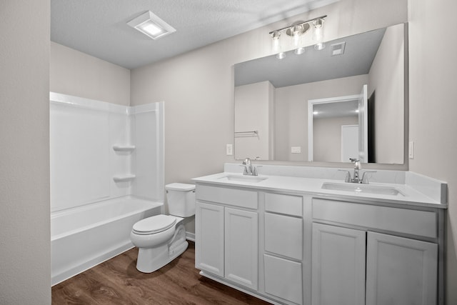 bathroom featuring wood finished floors, toilet, double vanity, a textured ceiling, and  shower combination